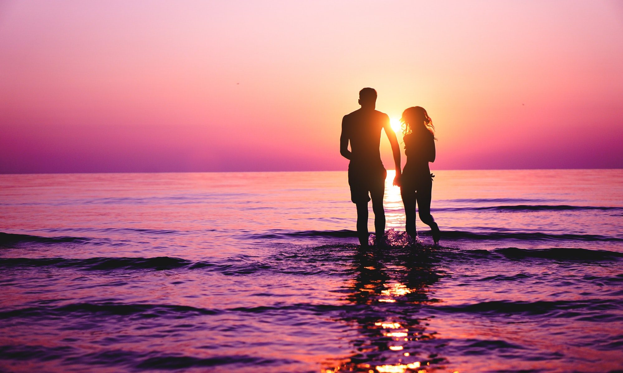 Silhouette of couple in love running inside ocean water at sunset